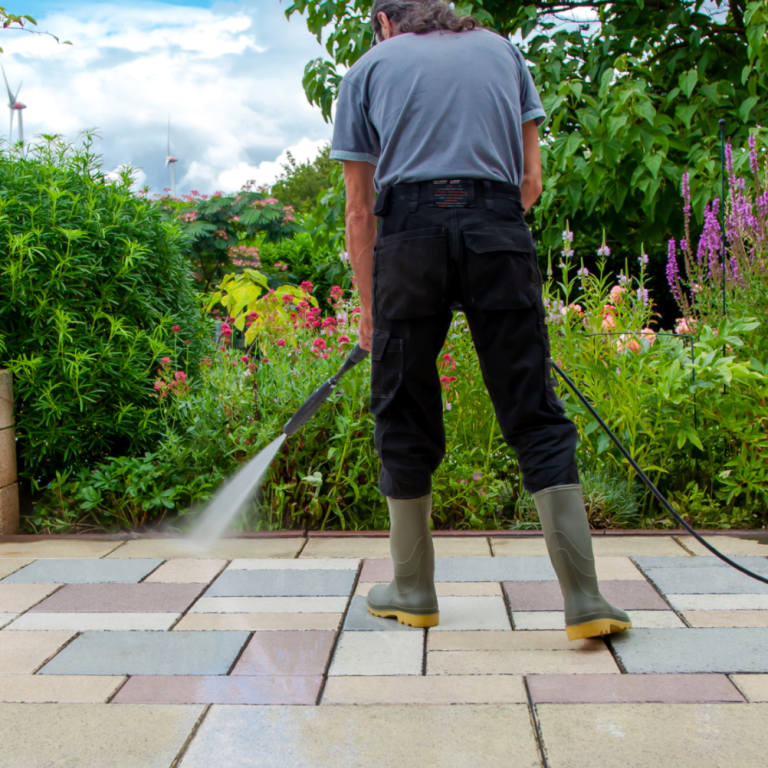 Person mit Gummistiefeln reinigt Pflastersteine mit einem Hochdruckreiniger im Garten.